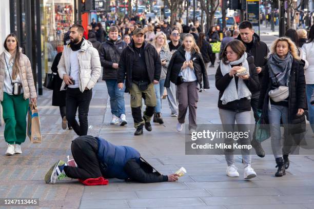 Homeless man kneels prostrate on the pavement begging for money while people pass by on Oxford Street on 6th February 2023 in London, United Kingdom....