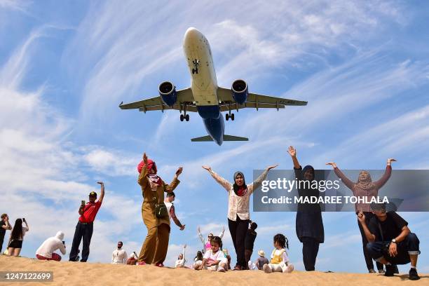 In this picture taken on February 13 tourists pose for picture on Mai Khao Beach as a plane lands at Phuket International Airport in Phuket province.