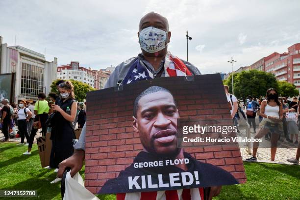 Black man wears his protective mask with an "I can't breathe" sentence while displaying a George Floyd portrait as protesters gather to demonstrate...