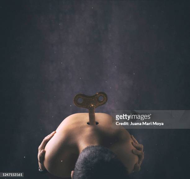 a young boy with a rope wrench on his back leaning in a lethargic pose.  concept of running out of energy - wind up toy imagens e fotografias de stock