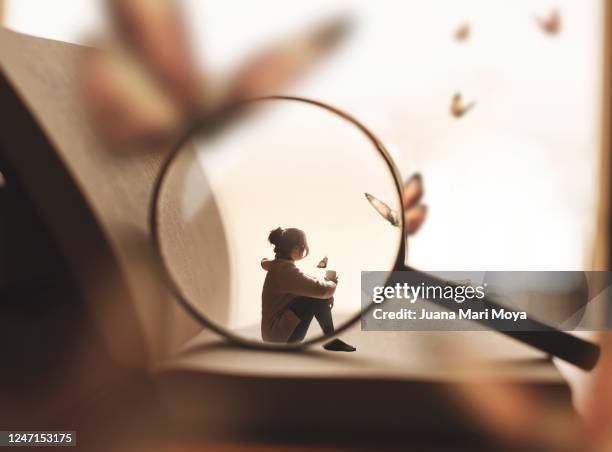 a woman sitting on a giant book having a cup of coffee.  she is dreaming of butterflies.  there is also a magnifying glass that is focusing on it. - cuento de hadas fotografías e imágenes de stock