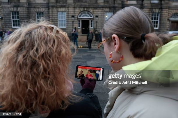 People watch a press conference held by Scotland's First Minister Nicola Sturgeon on a mobile phone as they gather stand outside of Bute House on...