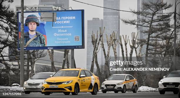 Cars roll past a billboard displaying Russian Army Warrant Officer Ilya Filippov, participating in Russia's military action in Ukraine, in central...