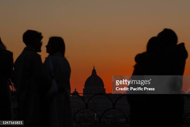 Couples watch the sunset from the promenade near Pincio Terrace on Valentine's Day, with St. Peter's Dome in the background.