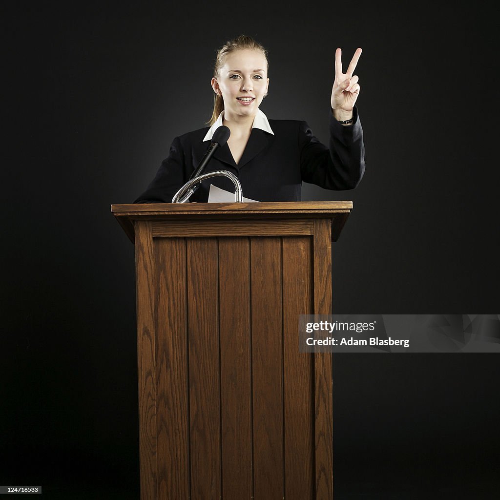 Young businesswoman giving speech at podium while giving the peace sign