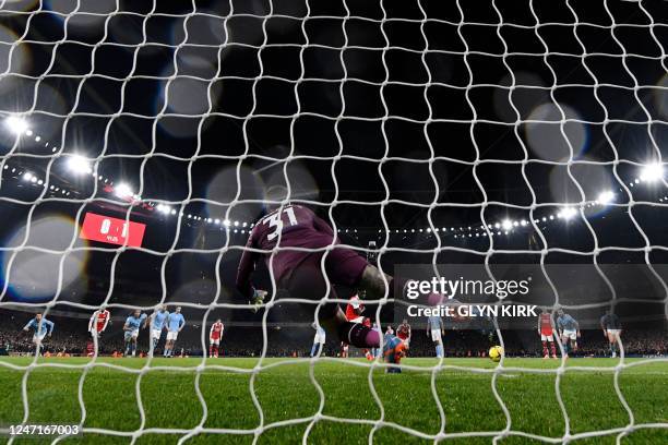 Arsenal's English midfielder Bukayo Saka shoots a penalty kick and scores past Manchester City's Brazilian goalkeeper Ederson during the English...