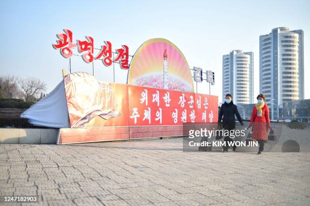 People walk along Changjon Street past a celebrative poster that translates as "Great General is the eternal sun of Juche" displayed as the country...