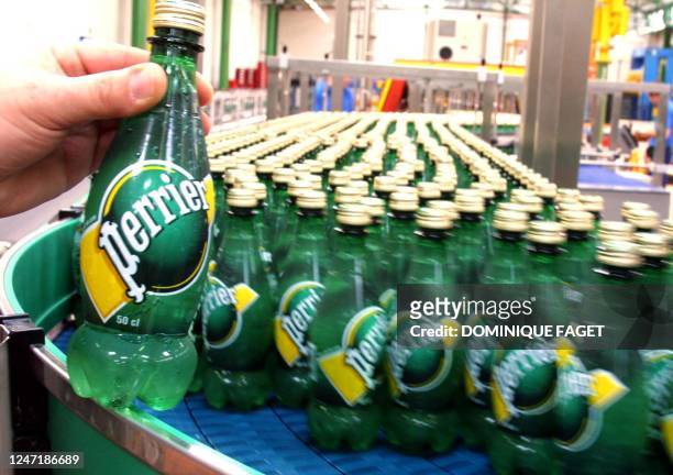 Un employé présente, devant la chaîne d'embouteillage, la nouvelle bouteille Perrier en plastique à Vergeze le 17 mai 2001. Cette nouvelle bouteille...