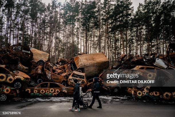 Woman pushes a baby stroller while walking in a cemetery of damaged civilian cars in the town of Irpin, near Kyiv on February 16 amid the Russian...