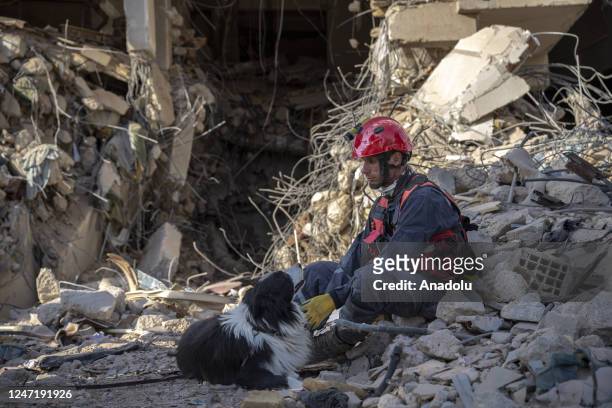 Search and rescue team sits on a pile of a debris with a dog as demolishing works and debris removal efforts continue in Antakya district after the...
