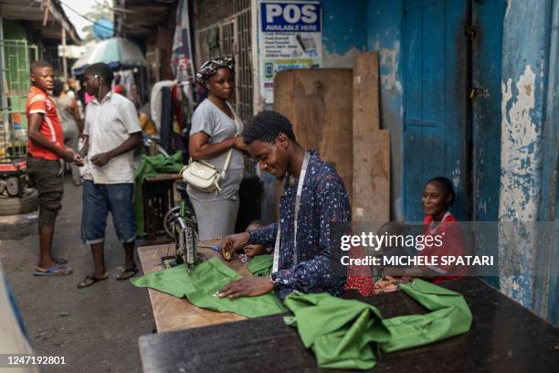 Street tailor sews a piece of canvas next to a sign advertising cashless payments in a market in Lagos on February 16, 2023. - Nigeria has been...