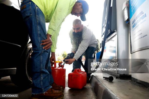 Gas customers Javier Tapia, left, and Ruben Hernandez, center, fill up gas cans in downtown Los Angeles on Thursday, February 16, 2023. The average...
