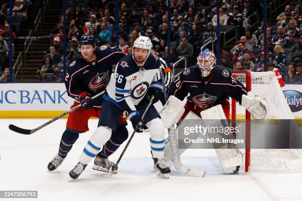 Andrew Peeke of the Columbus Blue Jackets and Blake Wheeler of the Winnipeg Jets battle for position in front of Joonas Korpisalo of the Columbus...