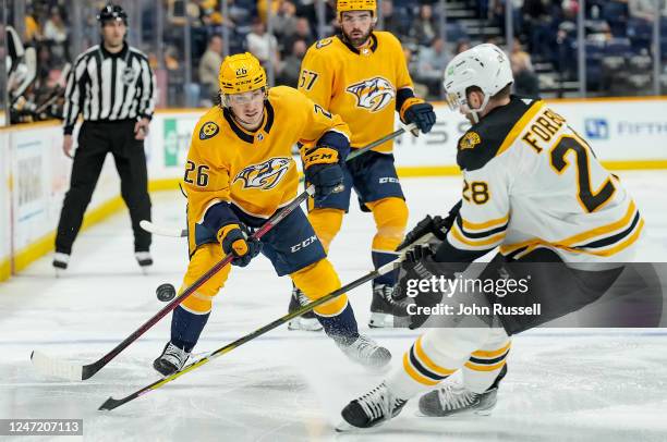 Philip Tomasino of the Nashville Predators passes the puck against Derek Forbort of the Boston Bruins during an NHL game at Bridgestone Arena on...