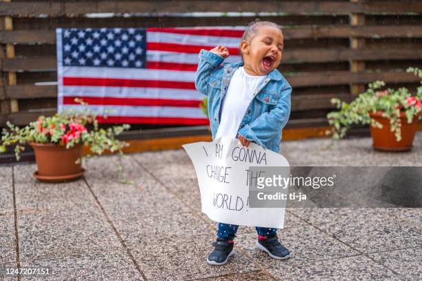 かわいい女の子が雨の中に立って、メッセージと拳とポスターを保持しています:私は世界を変えるつもりです! - racism ストックフォトと画像