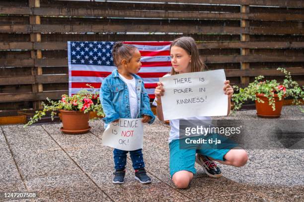 two girls holding posters with anti-racist messages outdoors in the rain - anti racism children stock pictures, royalty-free photos & images
