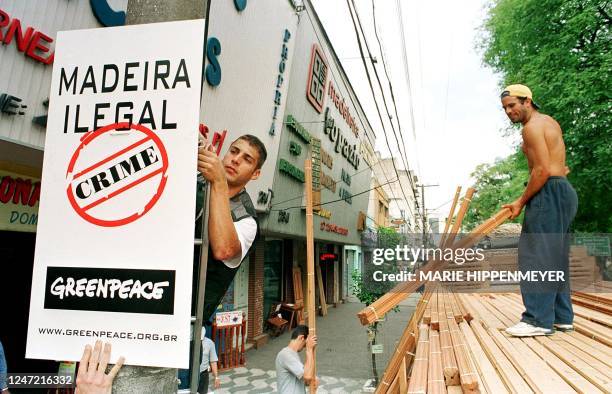 Greenpeace activist hangs a sign in Sao Paulo 15 December calling attention to the illegal wood being cut in the Amazon, while a worker unloads wood...