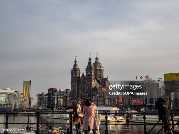 Two tourists are seen taking photos close to one of the canals in the city. Amsterdam is one of the most beautiful, creative, and cycle-friendly...