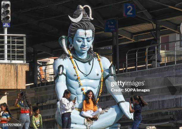 Girl is seen sitting on the lap of the statue of Hindu god Shiva on the roof of a temple on the occasion of Mahashivratri in Mumbai. Mahashivratri is...