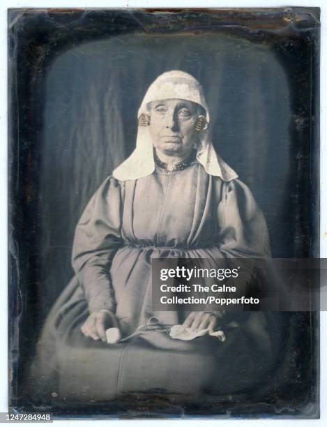 Vintage 19th Century Dutch Daguerreotype studio portrait of a woman wearing traditional costume and holding knitting yarn, she wears a long sleeved...