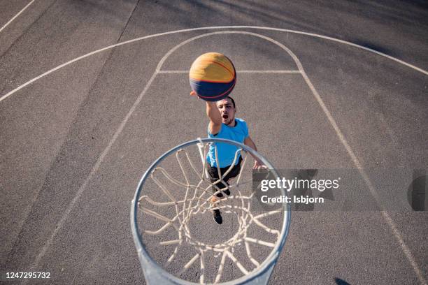 young man jumping and making a fantastic slam dunk playing street ball. - match basket stock pictures, royalty-free photos & images