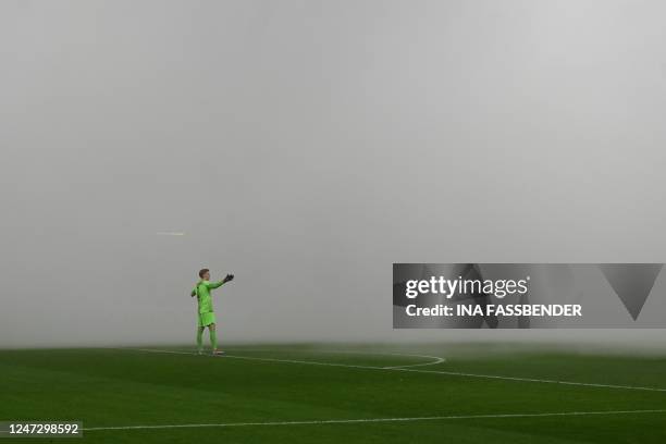 Hertha Berlin's Danish goalkeeper Oliver Christensen gestures as the pitch in engulfed in smoke from firworks lit my fans during the German first...