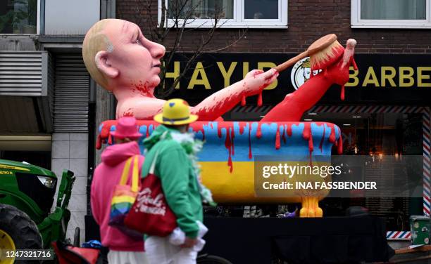 Carnival fool walks past a carnival float featuring Russia's President Vladimir Putin taking a blood bath in a bathtub in the colors of Ukraine...