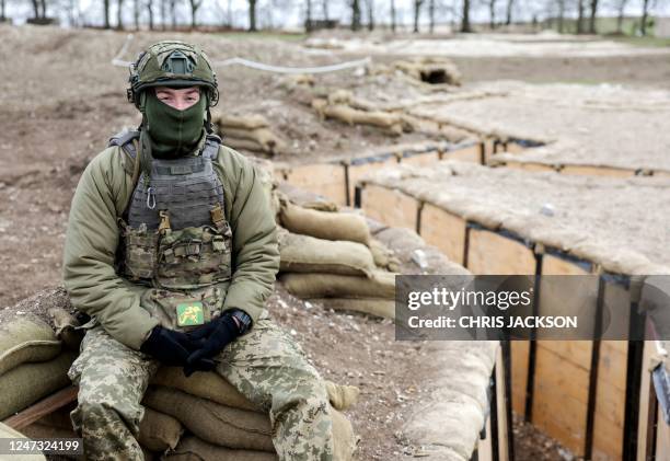 Ukrainian soldier poses for a photograph sitting beside a network of trenches, used in the training Ukrainians by British troops, in Wiltshire, south...