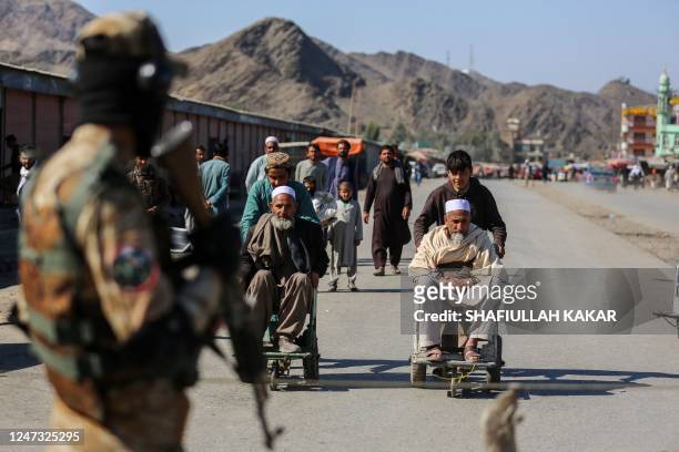 Taliban security personnel stands guard as young Afghan boys help elderly men in wheelchairs after an incident of gunfire between Afghanistan and...