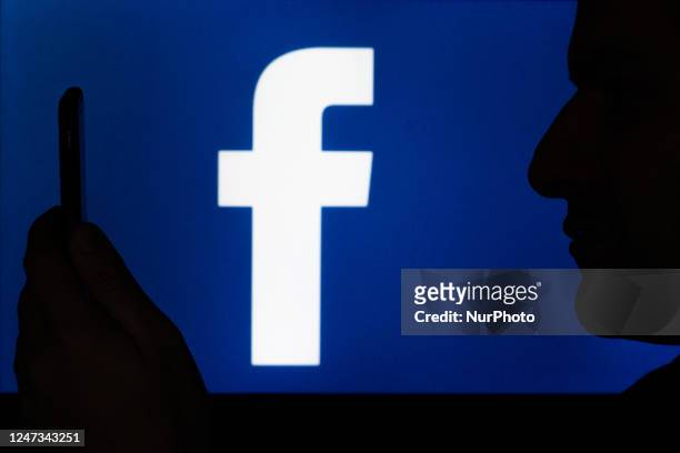 Facebook logo background behind a man using his smartphone is seen on February 20, 2023 in L'Aquila, Italy. Meta CEO Mark Zuckerberg announced the...