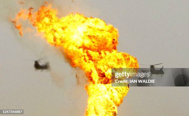 Military helicopters fly past a burning oil well at the Rumayla Oilfields 23 March, 2003 in Iraq. Several oil wells have been set ablaze by...