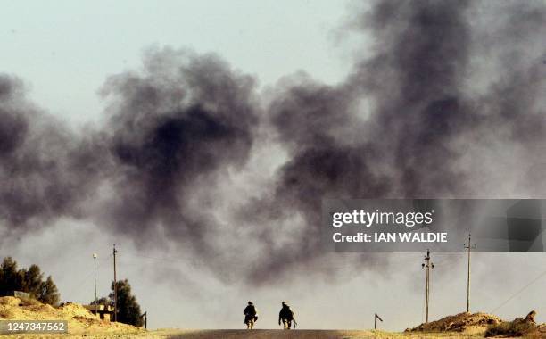 Soldiers from 1st Marine Expedition Force patrol a road as heavy black smoke from a burning oil well drifts past at the Rumaila Oilfields March 23,...