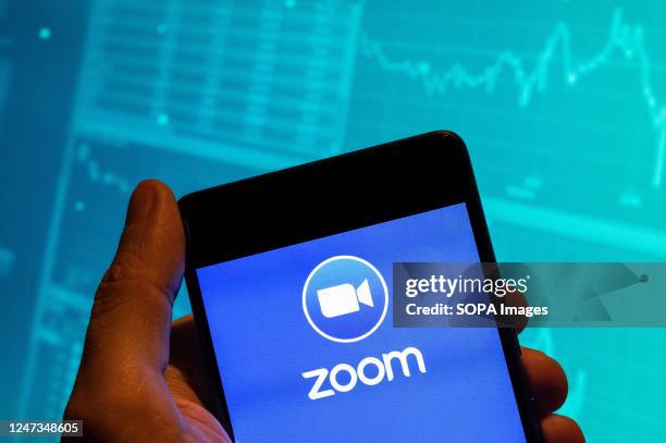 In this photo illustration, the American video Communications company Zoom logo is seen displayed on a smartphone with an economic stock exchange...