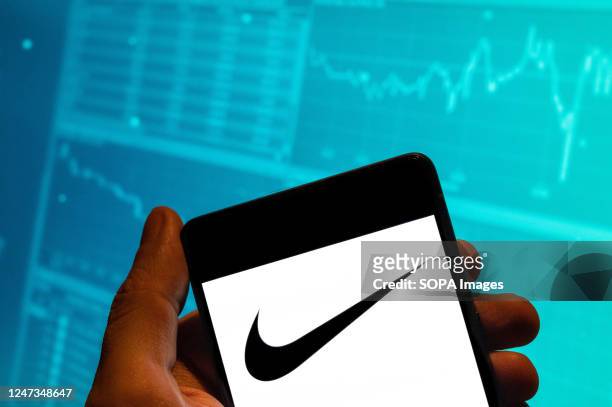 In this photo illustration, the American multinational sports clothing brand Nike logo is seen displayed on a smartphone with an economic stock...