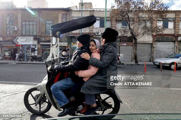 Man transports a girl and a woman in a motorcycle in Tehran on February 21, 2023. - Iran's currency plunged to new lows on January 20 amid fresh...