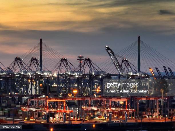 Long Beach, CA Cranes move shipping containers at the Port of Long Beach with a view of the International Gateway Bridge in the background at sunset...