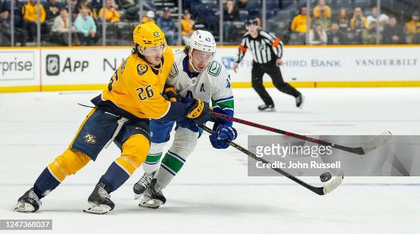 Philip Tomasino of the Nashville Predators battles for the puck against Quinn Hughes of the Vancouver Canucks during an NHL game at Bridgestone Arena...