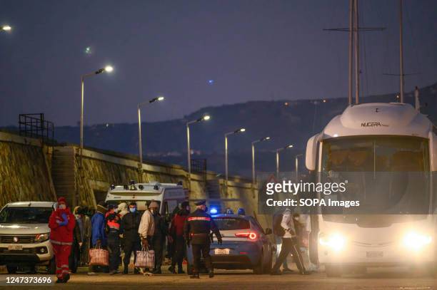 Police and Coastguard members seen near migrants as they board a bus. The Italian Coastguard rescue vessel "Dattilo" arrived at the Reggio Calabria...
