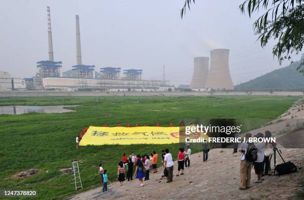 Greenpeace activists unfurl a banner condemning the use of coal, on a dry riverbed near one of the Beijing's biggest coal-fired power plants on July...