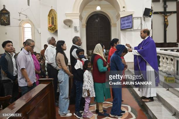 Catholic priest marks the symbol of the cross with ash on the forehead of a Christian believers during a mass on an Ash Wednesday service at a Church...