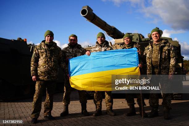 Ukrainian soldiers who are undergoing training at Bovington Camp, a British Army military base, pose with a Ukrainian flag in front of a FV 4034...