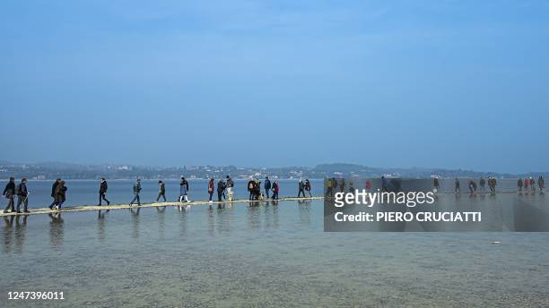 People walk towards the small island of San Biagio, off Manerba del Garda, Lake Garda, on February 21 where the water level dropped to its lowest in...