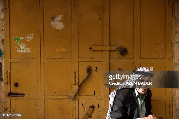 Man sits in front of a closed shop in a market area in the occupied West Bank city of Hebron on February 23 during a general strike called to protest...