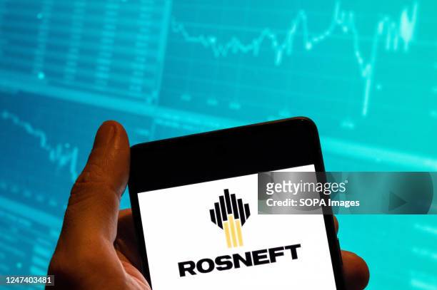 In this photo illustration, the Russian multinational oil and gas company Rosneft logo is displayed on a smartphone screen with an economic stock...