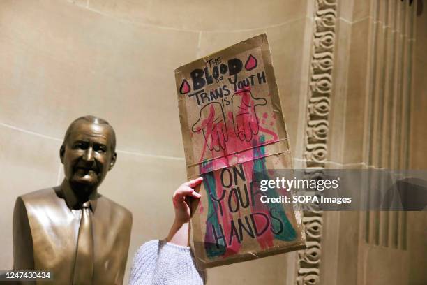 Protester holds a placard that says, "The blood of trans youth is on your hands" inside the Indiana Statehouse as the Indiana Senate's Health and...