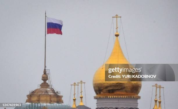 The Russian flag flies in the wind next to the domes of an Orthodox cathedral on the grounds of the Kremlin in central Moscow on February 24, 2023.