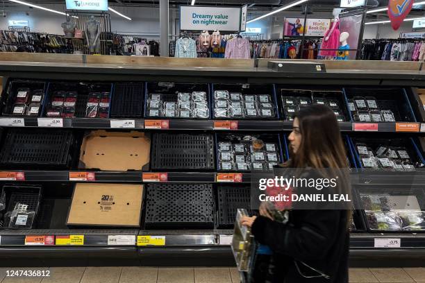 Customer walks past empty shelves at a Sainsbury supermarket, in east London, on February 24, 2023. - Some UK supermarkets have introduced limits on...