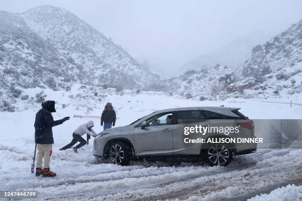 Person helps push out a vehicle that became stuck in the snow on a roadway in the San Gabriel Mountains in the Angeles National Forest, California,...