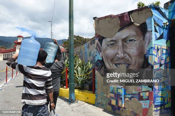 Men walk carrying jerrycans with water next to an aging mural depicting Venezuela's late President Hugo Chavez in the 23 de Enero neighborhood of...