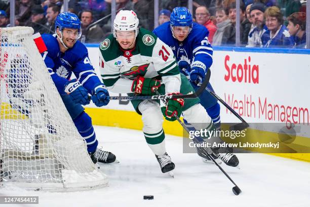 Brandon Duhaime of the Minnesota Wild plays the puck against Pierre Engvall and David Kampf of the Toronto Maple Leafs during the first period at the...